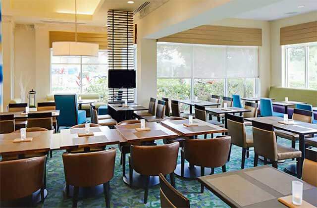 breakfast dining area with blue chairs windows and tv at hilton garden inn orlando international drive north