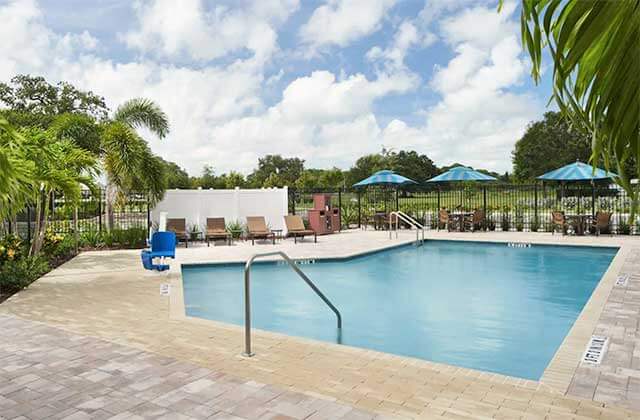 brick patio pool area with blue umbrellas palm trees and cloudy sky at hyatt place melbourne palm bay florida