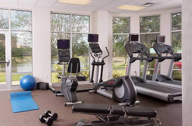 fitness center with cardio machines bench weights and lake view from windows at springhill suites orlando airport