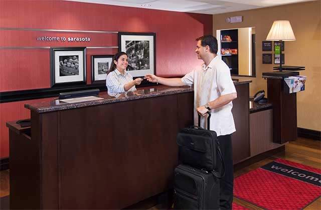 front desk with woman handing key card to man with suitcase at hampton inn suites sarasota lakewood ranch