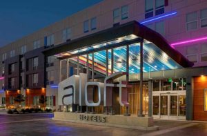 front entrance at exterior of hotel building at night with colorful neon lighting at aloft orlando international drive