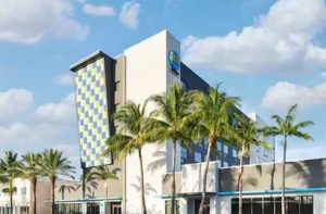 front exterior of blue yellow and white hotel building with palm trees at tru by hilton ft lauderdale airport