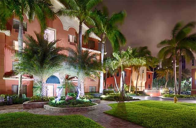 front exterior of hotel at night with uplighting and palm trees at best western plus palm beach gardens hotel and suites conference center