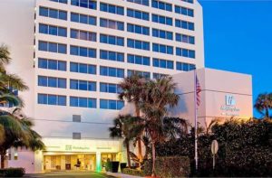 front exterior of high rise hotel with american flag and trees at holiday inn palm beach airport conference center