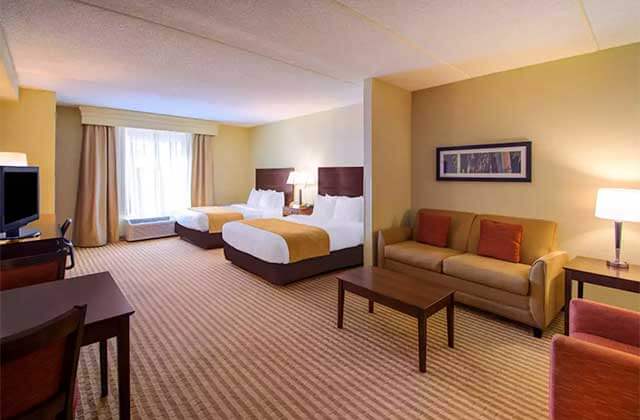 hotel room with two beds sofa desk and yellow accents at comfort suites near universal orlando resort