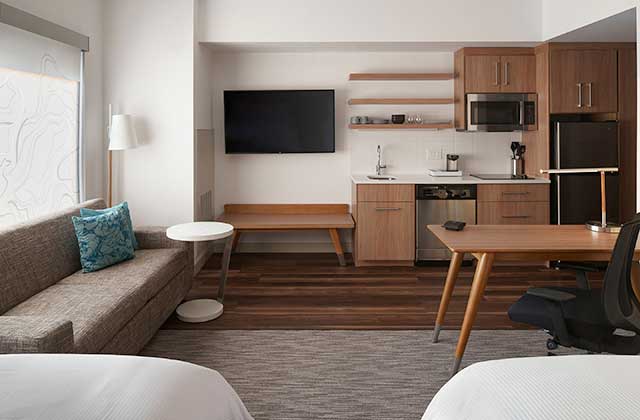 hotel room with two beds sofa kitchenette tv and dining area at element orlando international drive