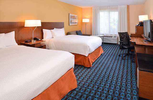 hotel room with two large beds desk window and sofa with orange and blue accents at fairfield inn orlando airport