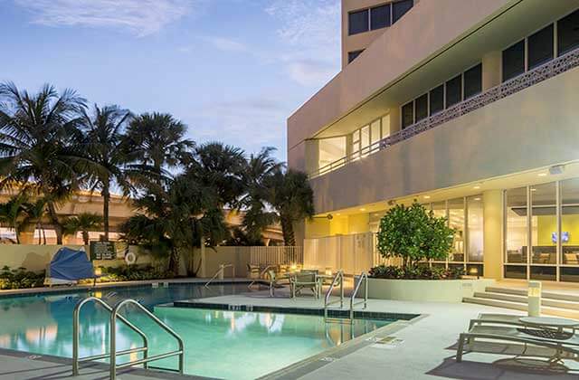 lighted green pool with palm trees at holiday inn palm beach airport conference center