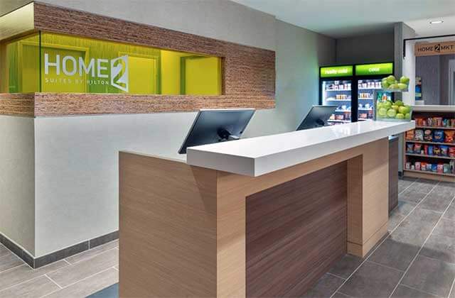 lobby and front desk with snack area and green accents at home2 suites by hilton orlando near universal