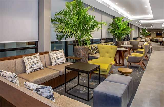 long lounge area with yellow wingback chairs brown sofas and plants at wyndham garden ft lauderdale airport and cruise port