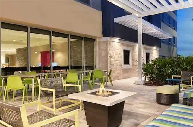outdoor patio area with firepit white trellis and palms at home2 suites by hilton palm bay i-95