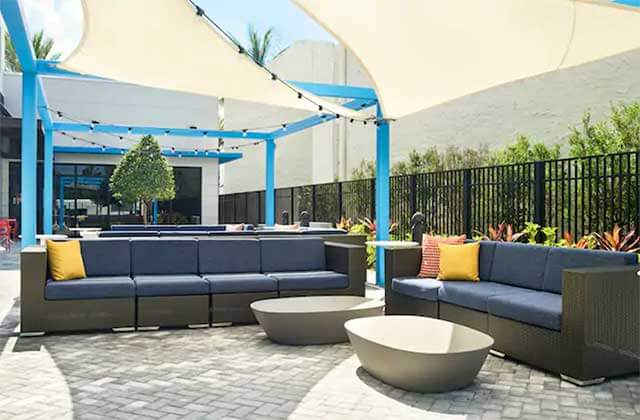 outdoor patio area white canopies blue seating areas and landscaping at tru by hilton ft lauderdale airport