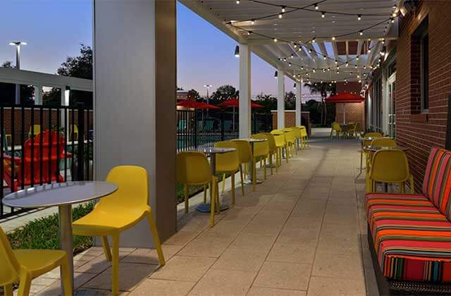 outdoor patio at twilight with string lights and yellow and orange seating at home2 suites by hilton orlando near ucf