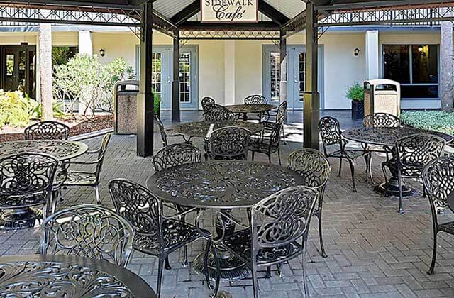 outdoor tables and chairs in a covered dining area with sign that reads sidewalk cafe at staybridge suites orlando royale parc suites