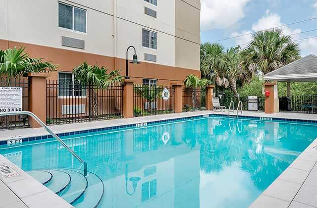 pool area with black iron fence and beige hotel building at candlewood suites fort myers sanibel gateway