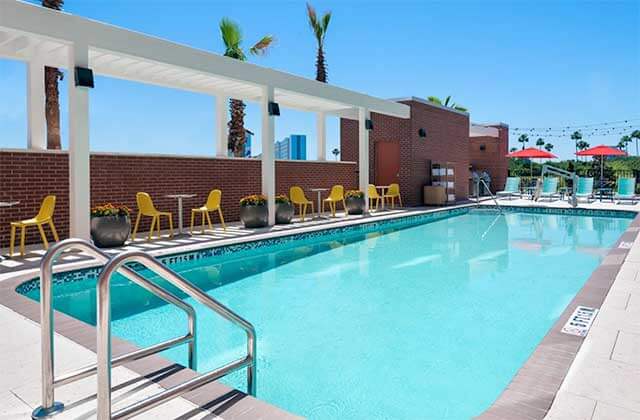 pool area with white trellis and yellow and blue chairs at home2 suites by hilton orlando near universal