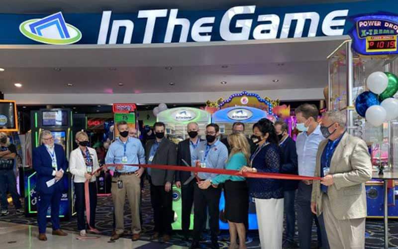 row of business men and women with face masks standing behind a red ribbon for in the game arcade opening at icon park orlando