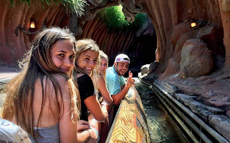 three young women and a man ride in a log water ride approaching a tunnel