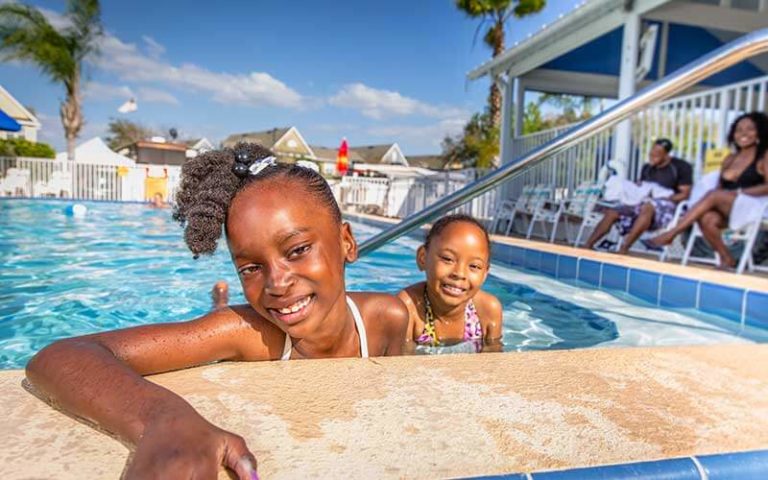 two girls smiling in swimming pool with people in chairs at orlando kissimmee koa holiday