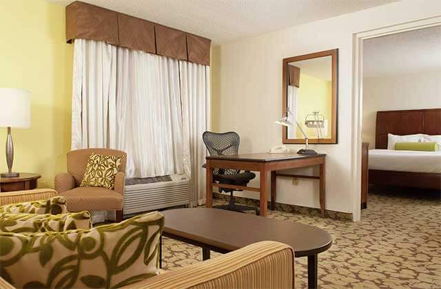 two room hotel suite with yellow decor bed desk and sofa at hilton garden inn orlando airport