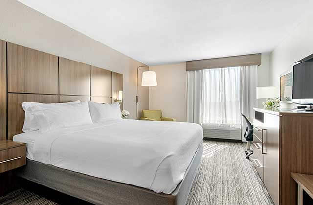 upscale hotel room with king size bed desk lamp chair dresser and tv at holiday inn melbourne viera conference center