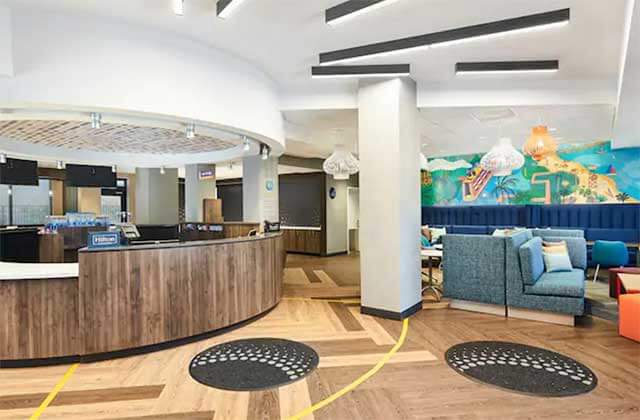 upscale lobby with round reception desk wood panel floor and blue sofas at tru by hilton ft lauderdale airport