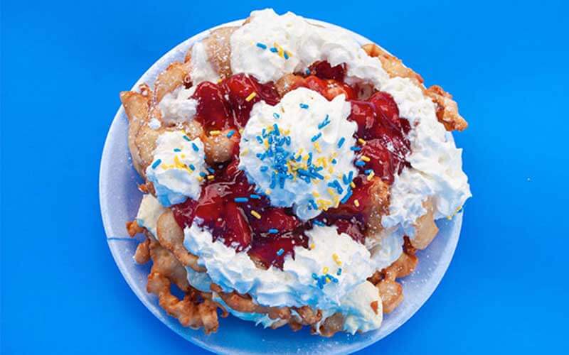 a funnel cake topped with strawberries and whipped cream with blue sprinkles celebrate fourth of july at fun spot america orlando theme park