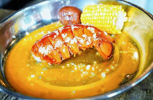 buttered lobster tail with cob corn and potato in a steel bowl at the juicy crab orlando