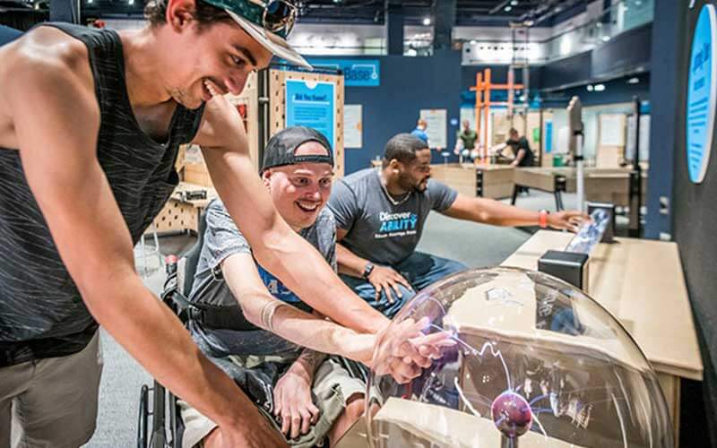 two young men one in wheelchair touch a plasma lamp exhibit at orlando science center