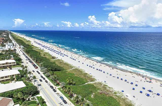 aerial view of long beach with row of blue umbrellas blue water cloudy sky coastal highway and hotels at delray beaches