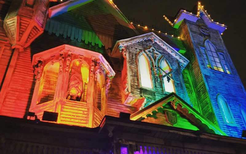 old looking run down mansion lit up with colorful lights red yellow green blue and violet at mortem manor haunted house halloween attraction at old town in kissimmee