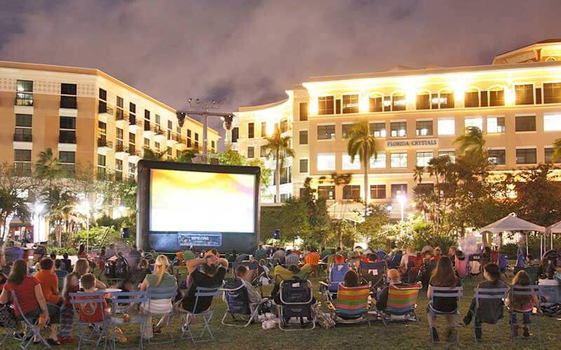 crowd at night with lawn chairs watching large screen film with downtown buildings at screen on the green event for fall fun in west palm beach blog