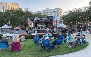 crowds seated on lawn chairs watching band performing on stage in a park in daylight for fall fun in west palm beach blog