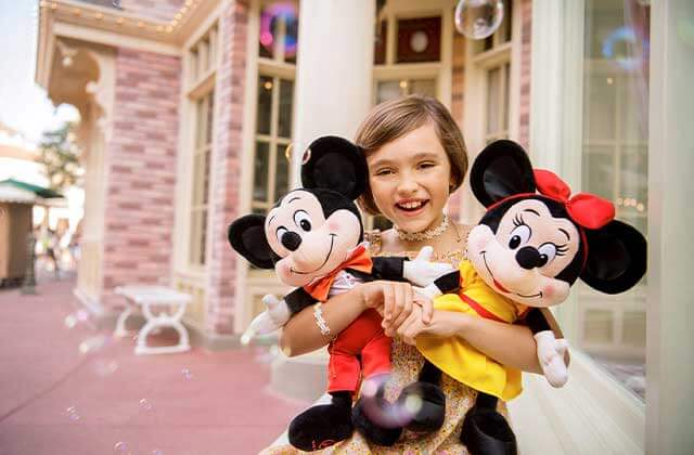 little girl in princess costume holding mickey and minnie plushes with bubbles in a theme park at walt disney world resorts