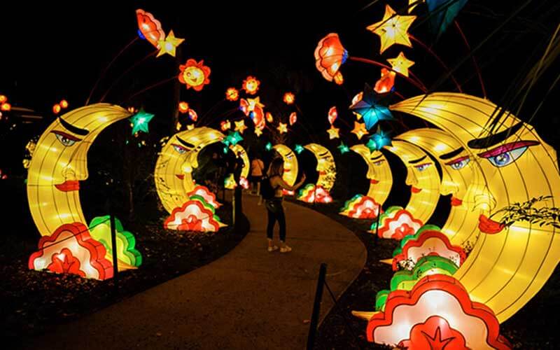 walkway at night with colorful lantern constructions of moons stars and flowers with woman taking photos for asian lantern festival at central florida zoo and botanical gardens sanford blog