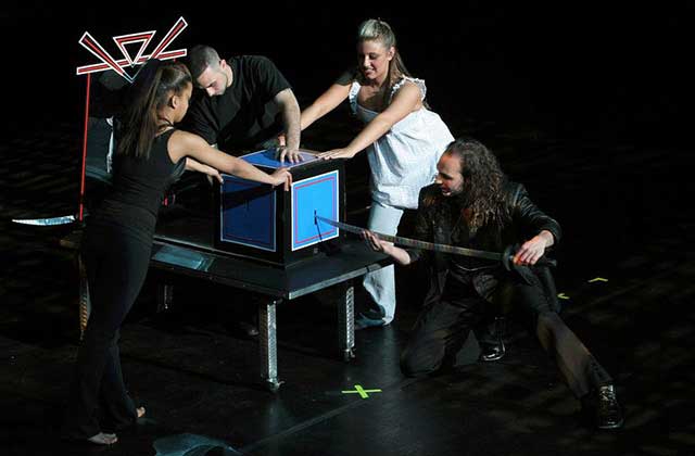 assistants hold box while illusionist puts sword into slot on stage at icons of magic show orlando