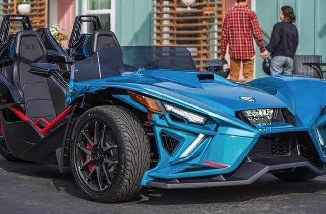 blue slingshot vehicle with couple in background with home at florida slingshots