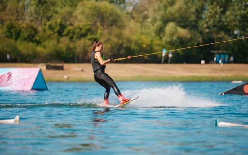 young adult female wakeboards on water surrounded by trees with obstacles in the water 