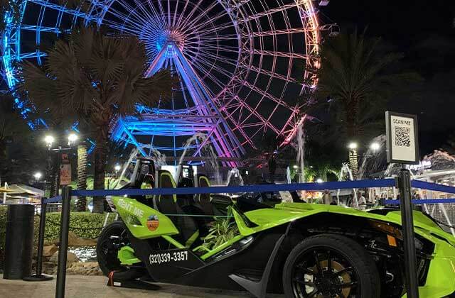 green slingshot at night parked in front of the wheel at icon park for central florida slingshots orlando