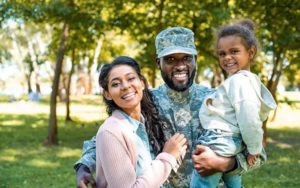 man in military uniform hugs wife and child with trees in background for orlando military discounts blog