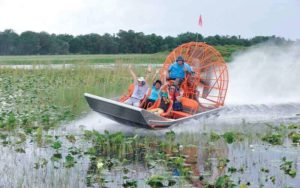 happy people sit on an airboat with an orange fan in a lake with lillypads surrounded by trees at Boggy Creek Airboat Adventures in Kissimmee