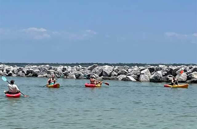 four kayakers paddle around the lagoon in front of the rock jetty at St. Andrews and Shell Island State Park in Panama City Beach, Florida.