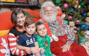 kids sit with santa claus character with tree and toy train decor at santa workshop experience in icon park for holidays in orlando blog