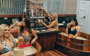 two wooden hot tubs with two girls in each drinking beer at beer spa orlando