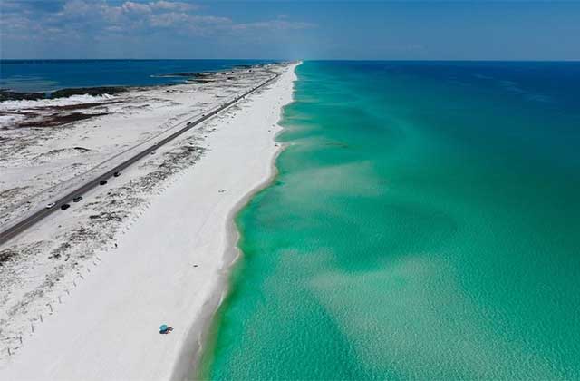 aerial view of the beach at St. Andrews and Shell Island State Park in Panama City Beach, Florida with crystal clear emerald blue water wide stretch of sugar white sand
