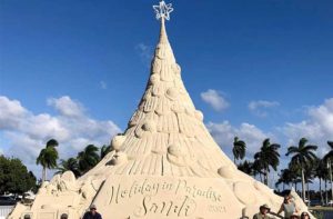 35 foot tall, 700 ton christmas tree made out of sand with large star on top, sand carvings of shells, holidays in paradise sandi etched into the base some people sitting at the base of the tree in West Palm Beach Florida