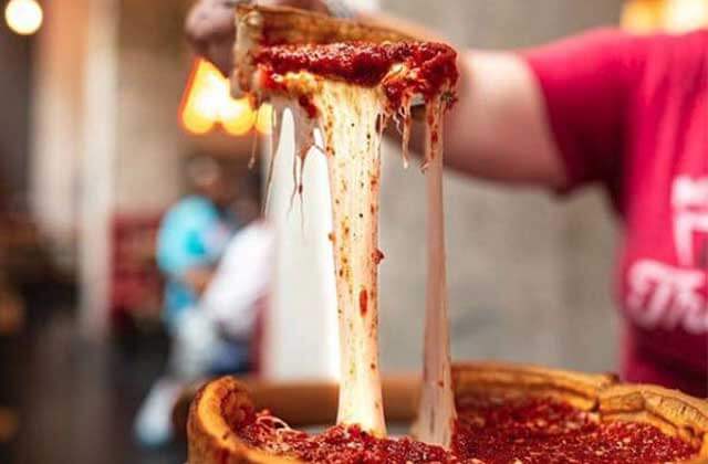 person wearing a red t shirt pulls a piece of giordanos pizza up with a string of cheese connected to the pizza at giordanos kissimmee