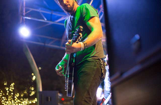 close photo of a guitar player from the crowd looking up at him wearing a green shirt at night at clematis by night west palm beach free concert