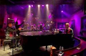 dueling piano players play for a crowd of people in a purple lit nightclub at jewel speakeasy orlando idrive