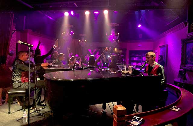 dueling piano players play for a crowd of people in a purple lit nightclub at jewel speakeasy orlando idrive